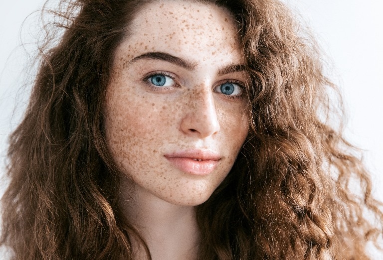 Beautiful Freckles young woman close up portrait. Attractive model with beautiful blue eyes and ginger curly hair