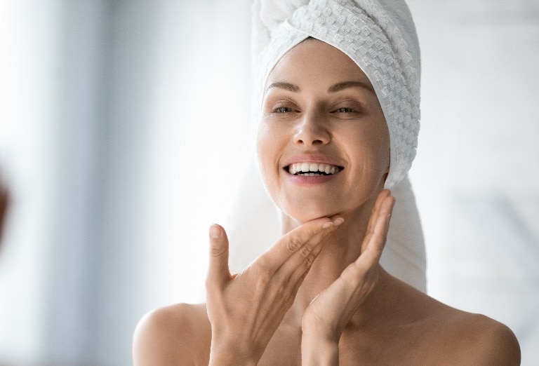 Happy lady look in bathroom mirror touching healthy face skin