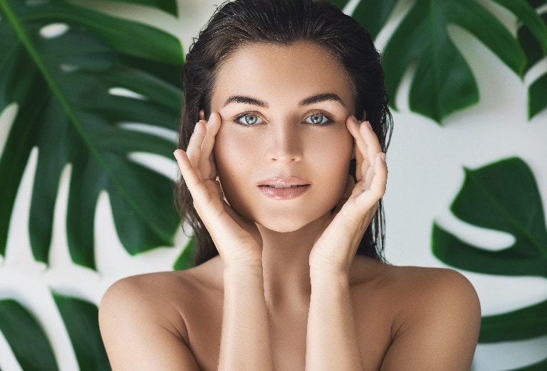 Portrait of young and beautiful woman with perfect smooth skin in tropical leaves