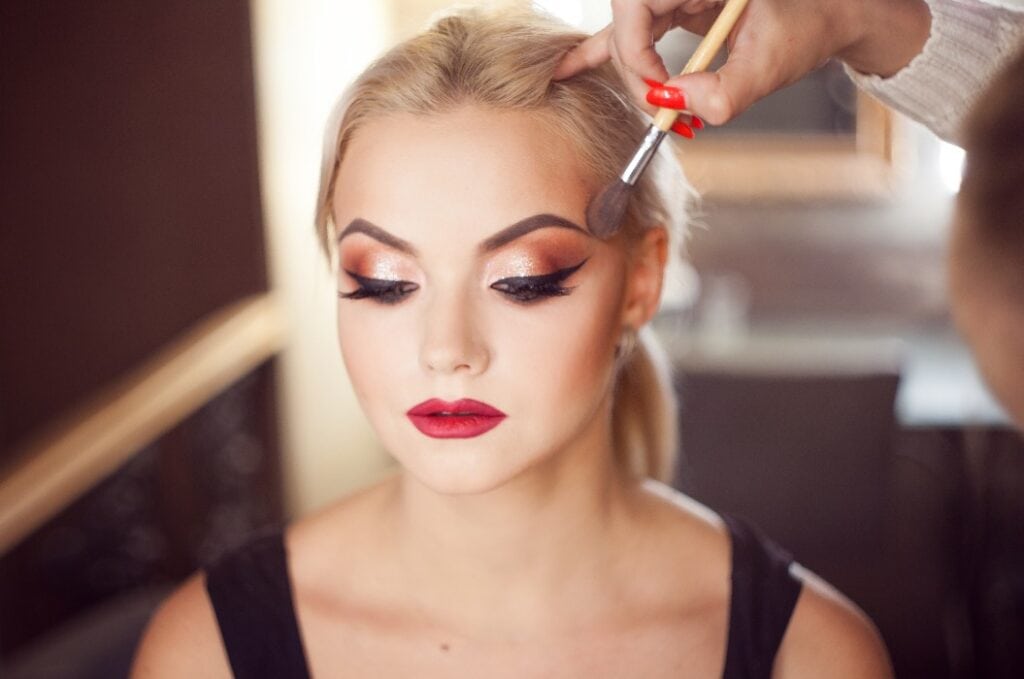 Beautiful young blonde. Makeup artist makes a stylish makeup.